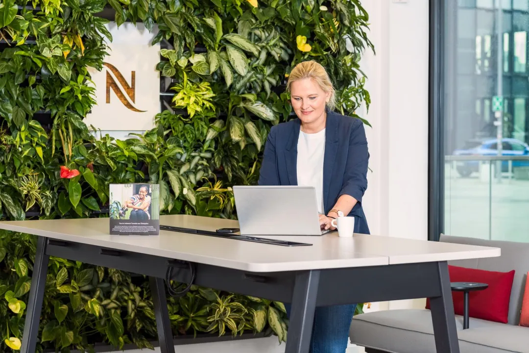 Female Nespresso Employee Standing at a Desk in Front of a Vibrant Green Wall, Focused on Her Work.