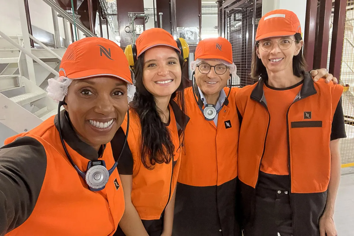 Four colleagues in orange caps and vests stand together smiling, proud to work in a manufacturing role at Nestle.