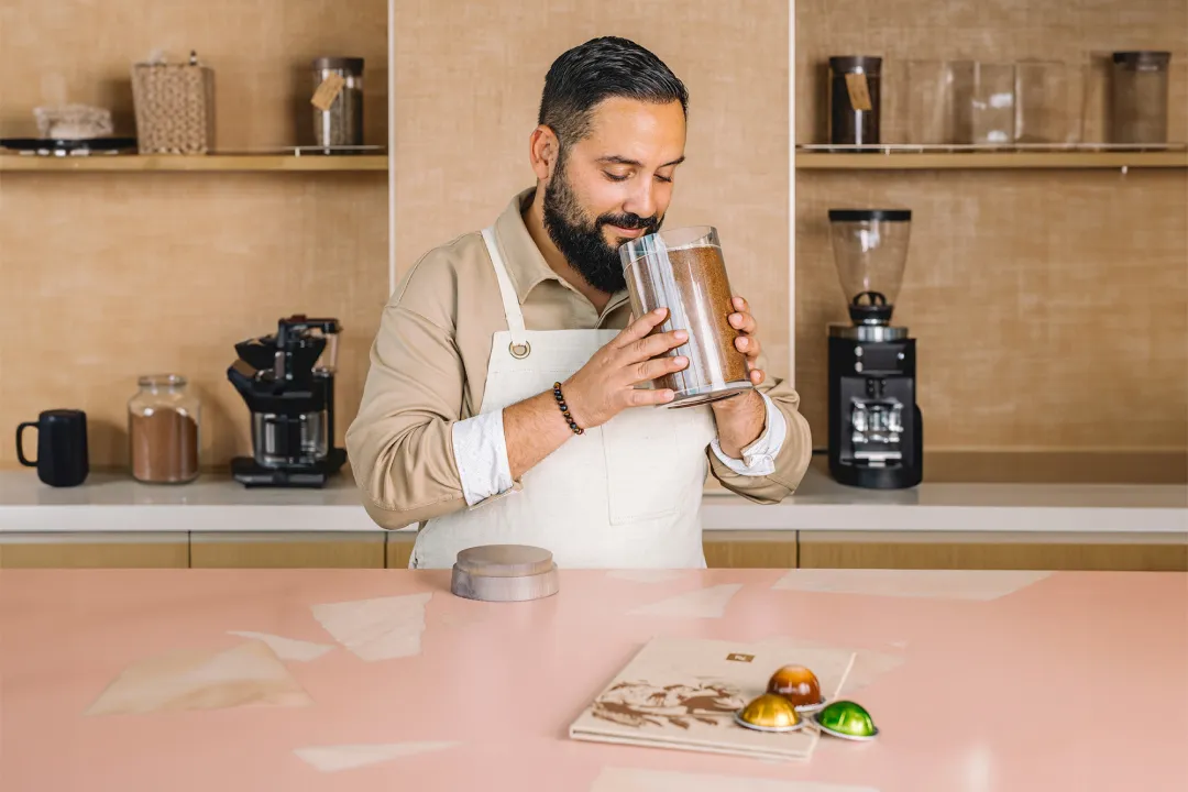 A Man in an Apron Holds a Container Filled With Coffee Granules in a Kitchen Setting.